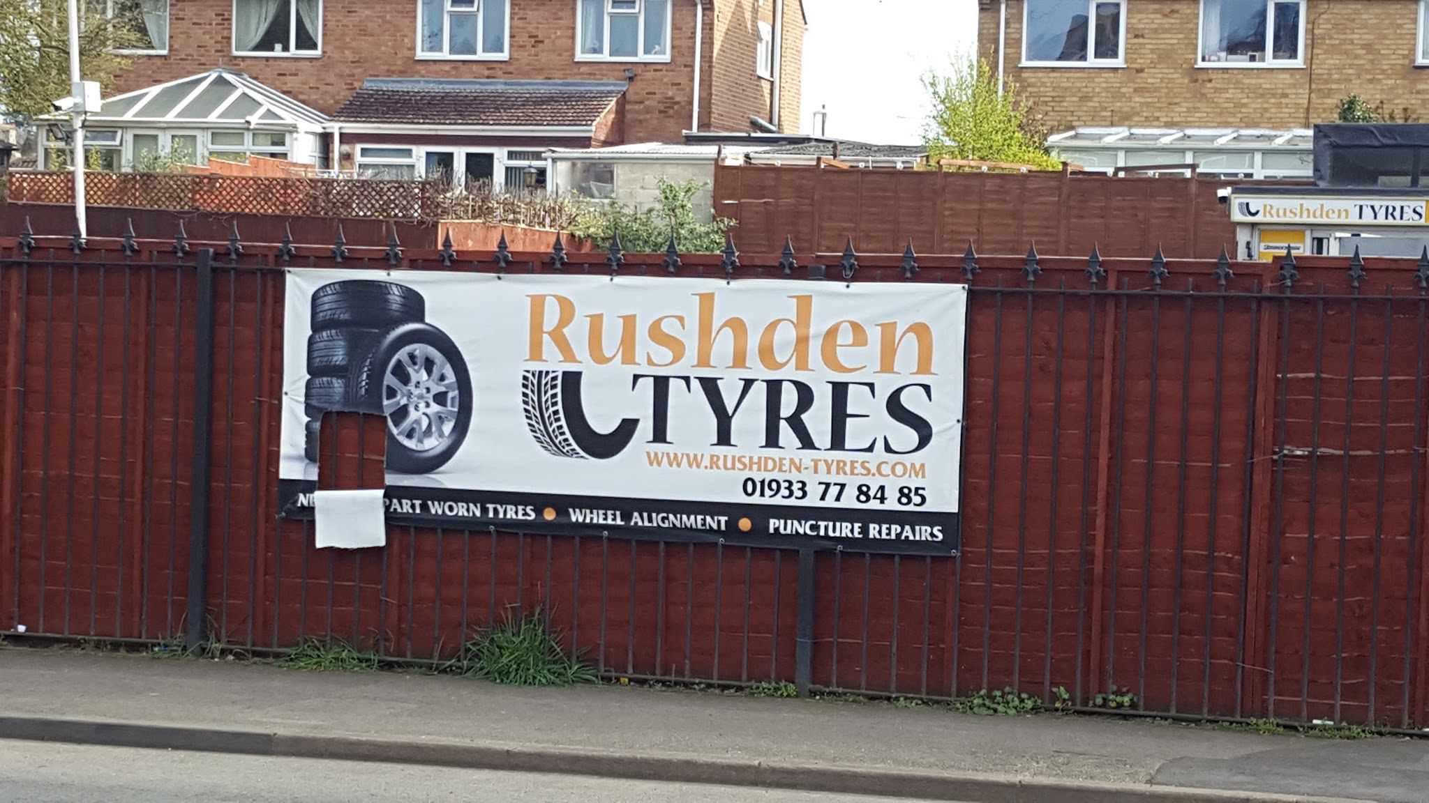 The Rushden Tyres roadside banner on a red fence: Part Worn Tyres, Wheel Alignment, Puncture Repairs